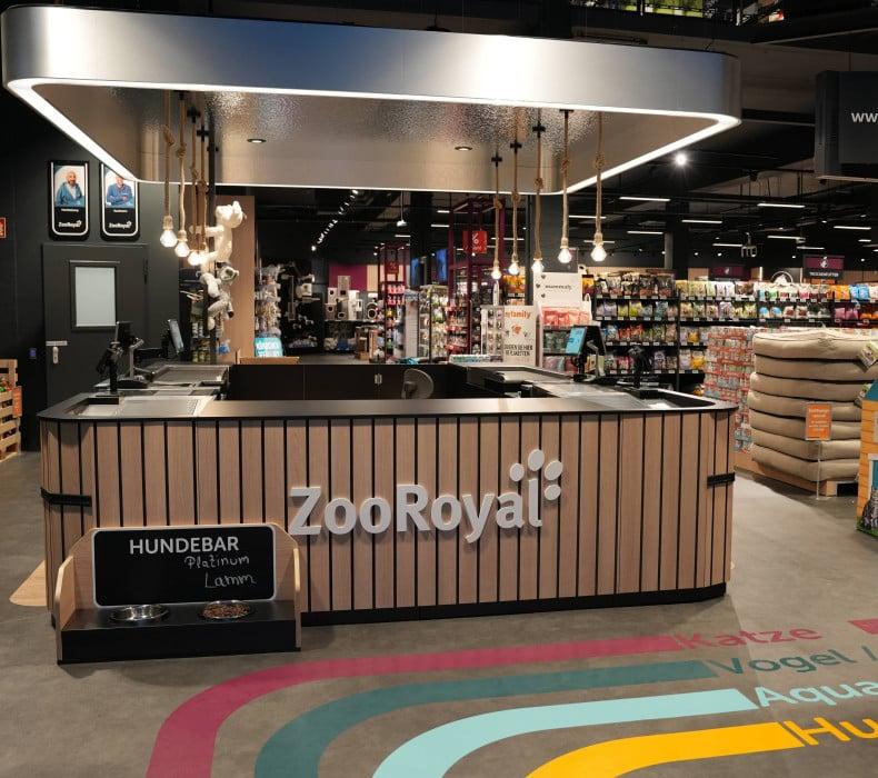 Kassenbereich mit Hundebar im ZooRoyal Fachmarkt Innenbereich eines ZooRoyal‑Shops mit einer Hunde‑Bar und Regalen voller Tierbedarf.
