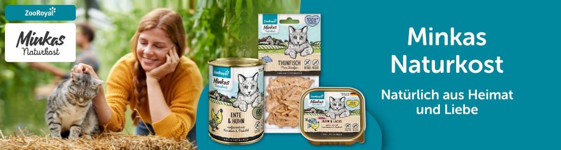 Minkas Naturkost Katzenfutter im Garten Katze sitzt auf Stroh neben einer Person, während Minkas Naturkost Katzenfutterprodukte daneben präsentiert werden.