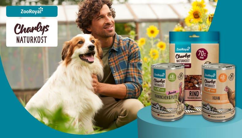 ZooRoyal Eigenmarken Charlys Naturkost Hund sitzt im Garten neben ZooRoyal Charlys Naturkost Produkten.