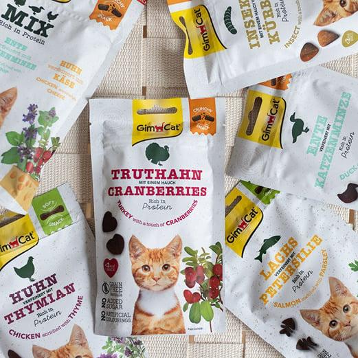GimCat Snacks Auswahl verschiedener GimCat Snacks in Beuteln, sortiert um eine zentrale Packung Truthahn Cranberries.