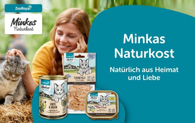 Minkas Naturkost Katzenfutter im Garten Katze sitzt auf Stroh neben einer Person, während Minkas Naturkost Katzenfutterprodukte daneben präsentiert werden.